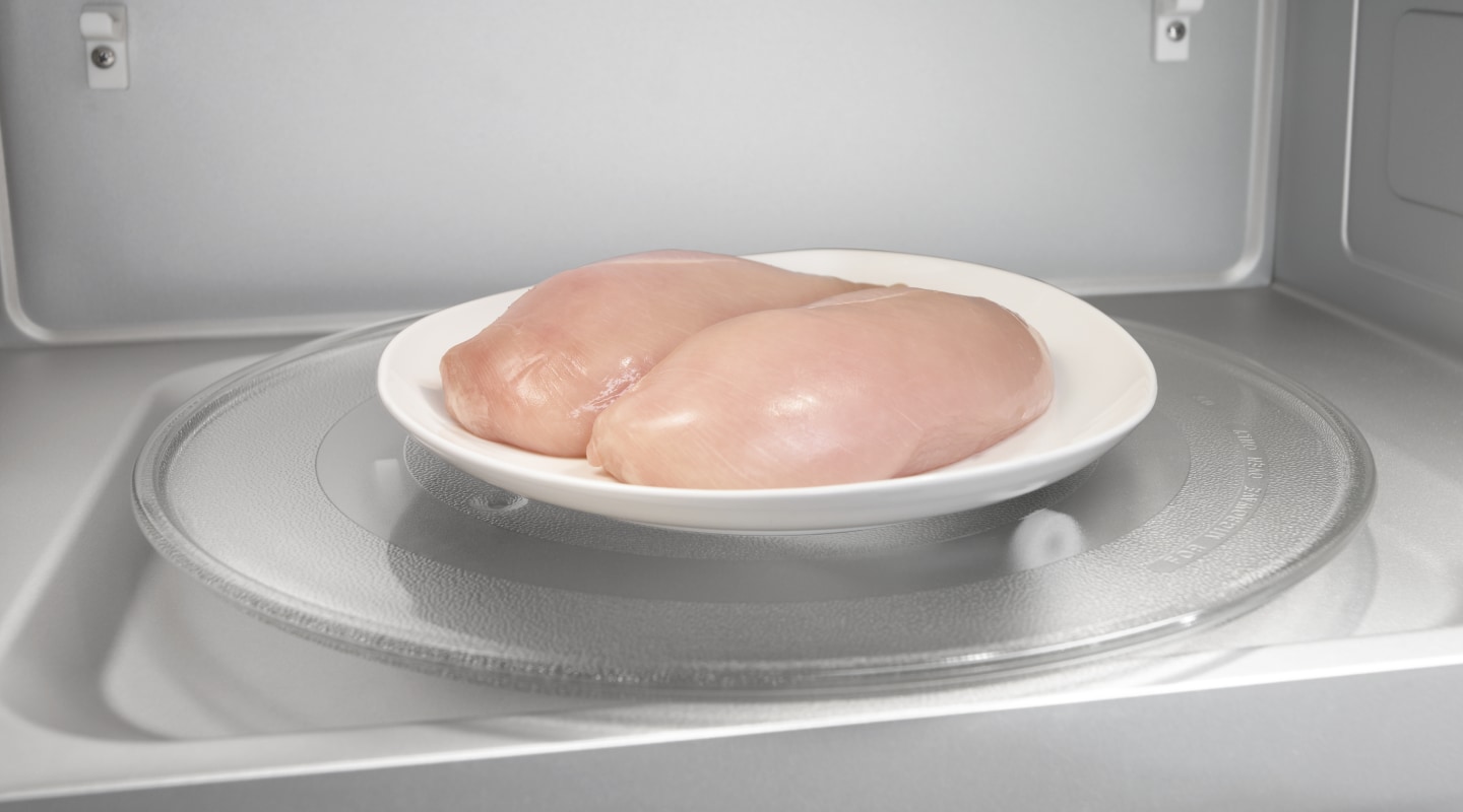 Two raw chicken breasts on a microwave-safe plate inside the microwave Two raw chicken breasts on a microwave-safe plate inside the microwave