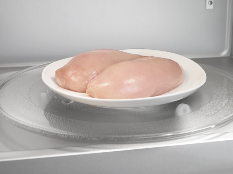 Two raw chicken breasts on a microwave-safe plate inside the microwave Two raw chicken breasts on a microwave-safe plate inside the microwave