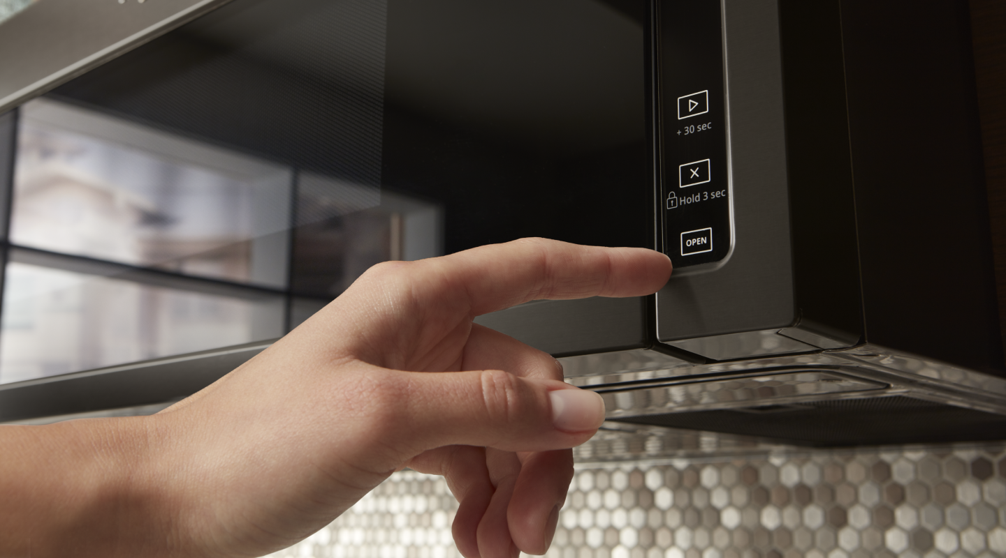 Person selecting the “open” button on an over-the-range microwave
