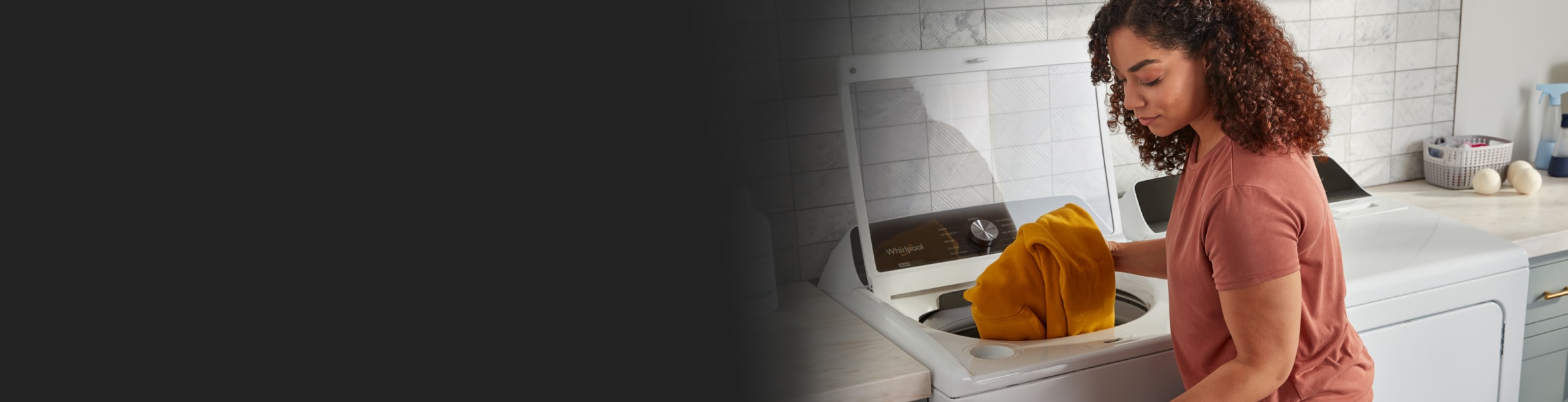 A person taking an orange sweater out of a top load washer.