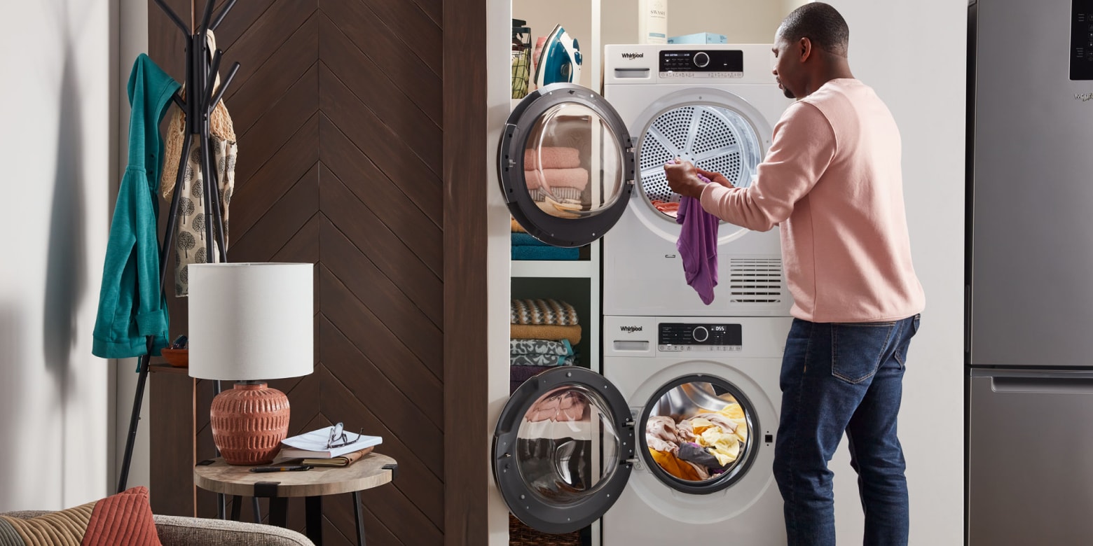 Man moving laundry from a stackable Whirlpool® front load washing machine down to the front load dryer below Man moving laundry from a stackable Whirlpool® front load washing machine down to the front load dryer below