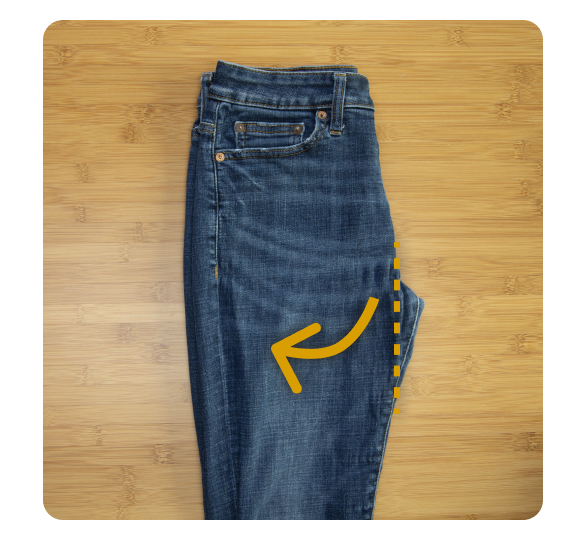 A pair of jeans folded in half with arrow directing fold under pants A pair of jeans folded in half with arrow directing fold under pants