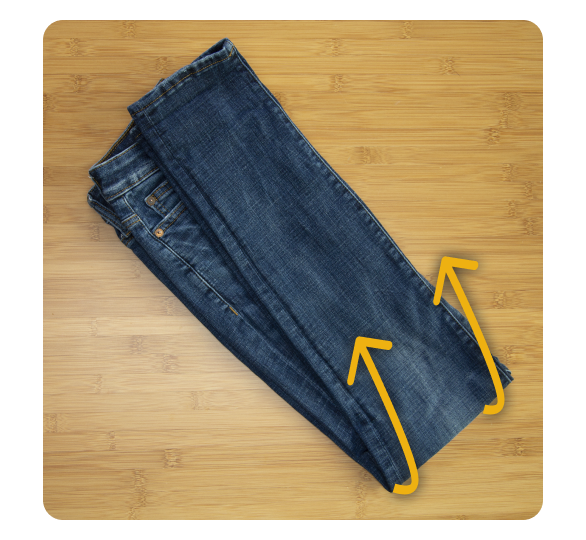 A pair of jeans folded in half with arrow directing fold under pants A pair of jeans folded in half with arrow directing fold under pants