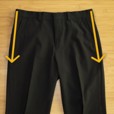 Creased pants laying flat on a table with arrows pointing down the sides