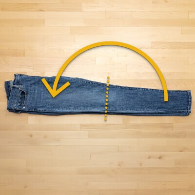 A pair of jeans folded in half, with arrows directing to fold in half lengthwise