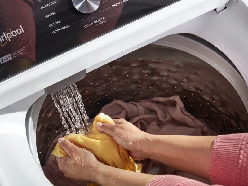 A person holding some laundry in the water stream of the washer as it fills A person holding some laundry in the water stream of the washer as it fills