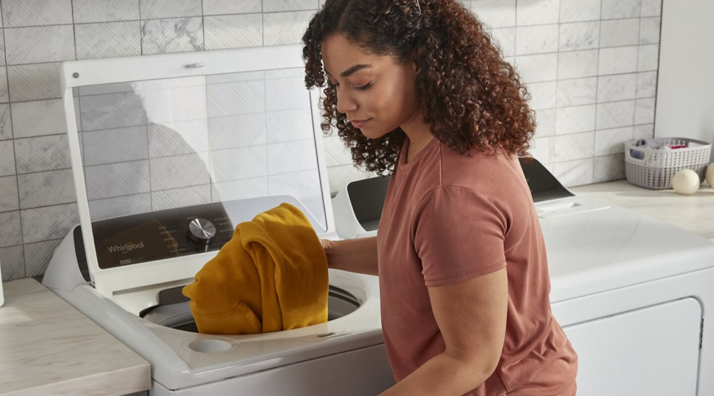 A person putting laundry in their washer A person putting laundry in their washer
