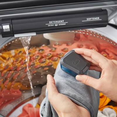Person spot treating clothing in front of a Whirlpool® Washing Machine