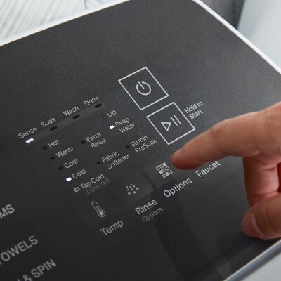 A finger hovering over cycle settings on a washer panel