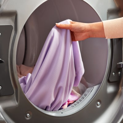 A hand holding a purple linen in the drum of a front load washer