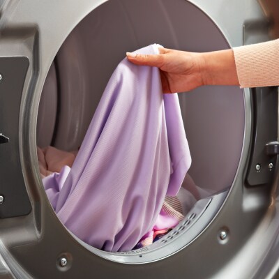 A hand holding a purple linen in the drum of a front load washer