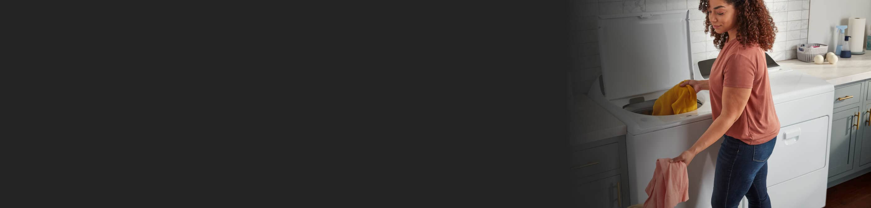 A person loading orange and pink linens into a white top load washer next to a white front load dryer