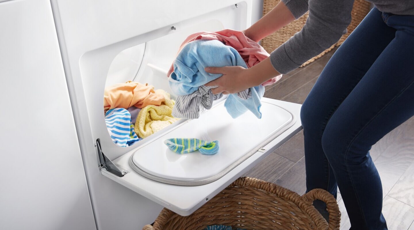 Person removing dry clothes from a dryer and placing them in a basket Person removing dry clothes from a dryer and placing them in a basket