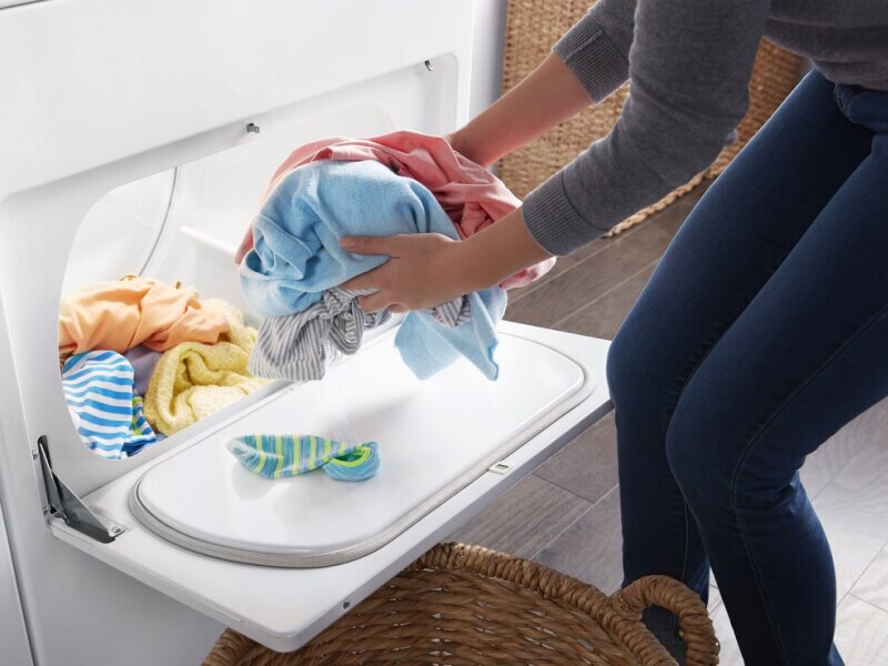 Person removing dry clothes from a dryer and placing them in a basket Person removing dry clothes from a dryer and placing them in a basket