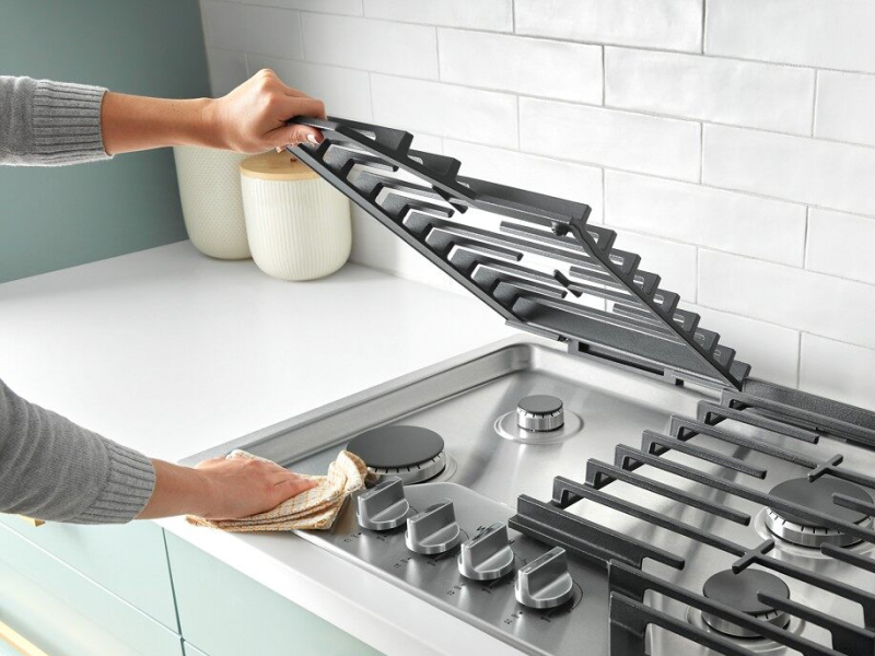 Hand lifting a grate on a gas cooktop