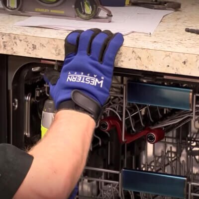 A blue glove gripping the counter above an opened dishwasher