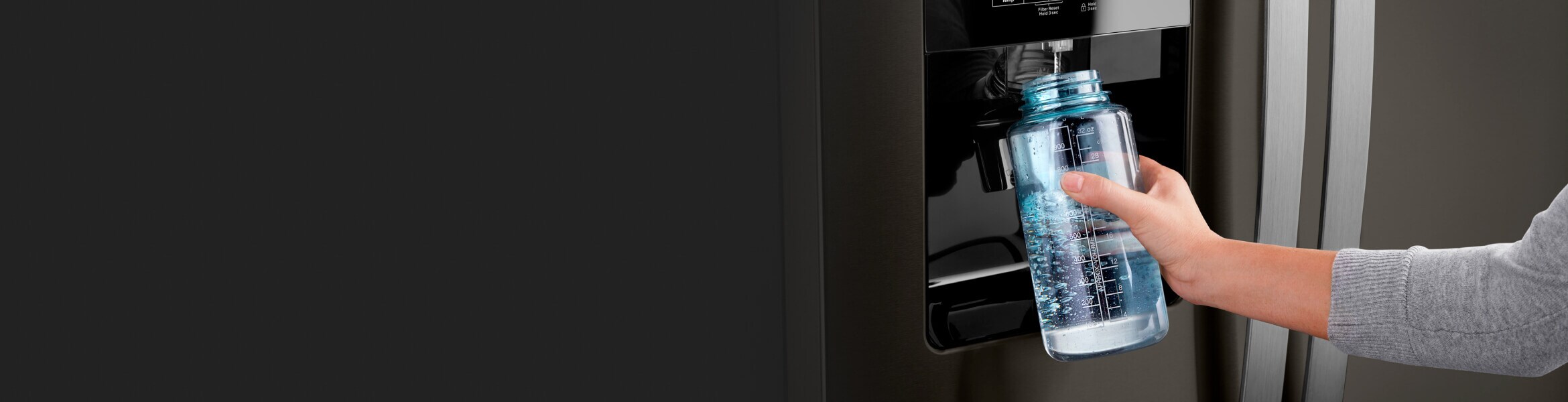 A person filling up their water bottle from the fridge