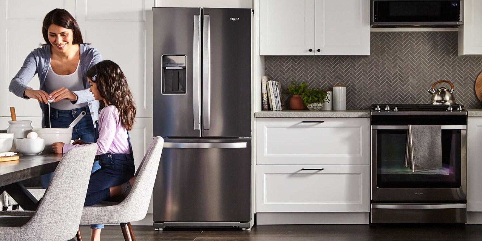 A woman and child cracking an egg into a bowl in a kitchen with a stainless steel refrigerator A woman and child cracking an egg into a bowl in a kitchen with a stainless steel refrigerator