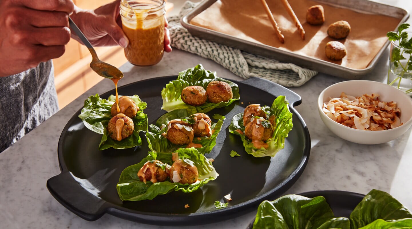 Person topping lettuce wraps with sauce Person topping lettuce wraps with sauce