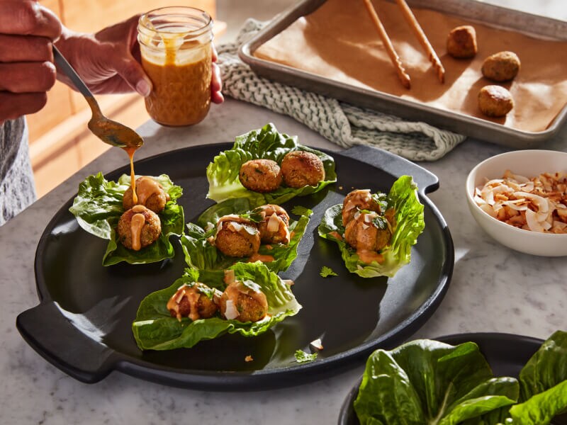 Person topping lettuce wraps with sauce Person topping lettuce wraps with sauce