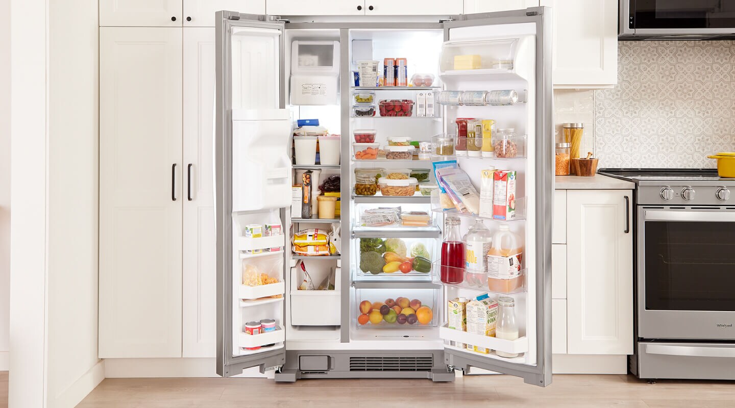 An open, side-by-side fridge filled with food and surrounded by white cabinets