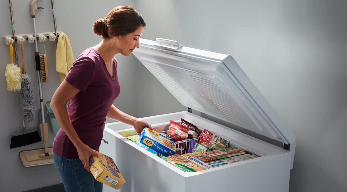 A person placing food in white chest freezer baskets