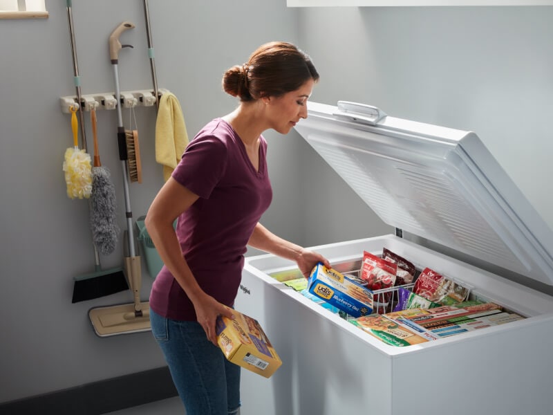 A person placing food in white chest freezer baskets