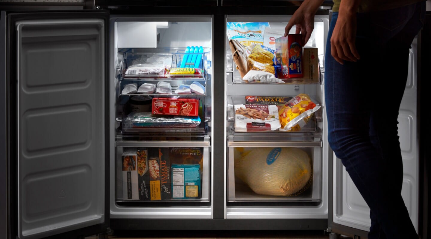 Side-by-side freezer drawers opened with person placing item in freezer