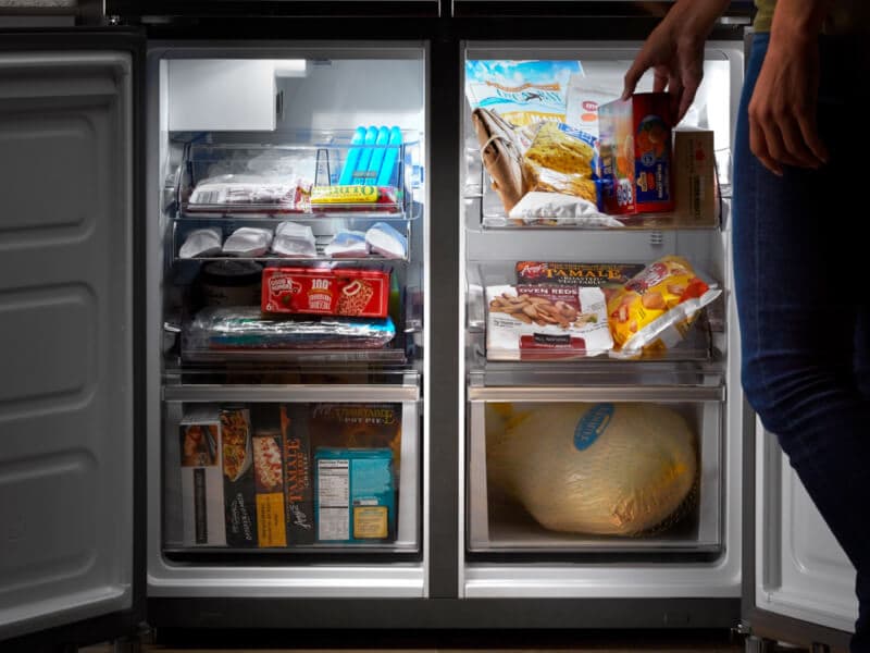 Side-by-side freezer drawers opened with person placing item in freezer