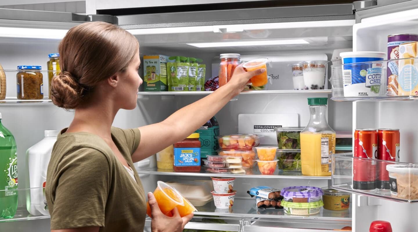 A person placing fruit cups into a refrigerator A person placing fruit cups into a refrigerator