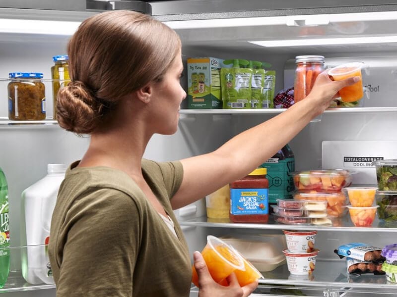 A person placing fruit cups into a refrigerator A person placing fruit cups into a refrigerator
