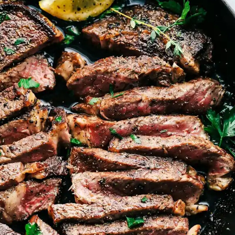 Thinly sliced steak pieces in a skillet garnished with a lemon wedge