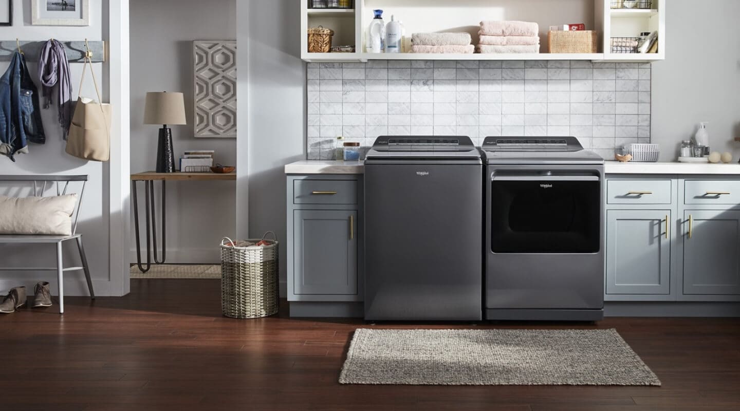 A laundry area with a grey top load washer and dryer by Whirlpool brand