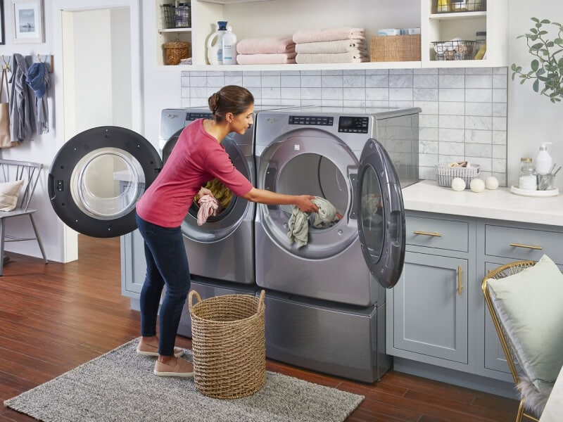 A woman moving clothes from her washer to her dryer