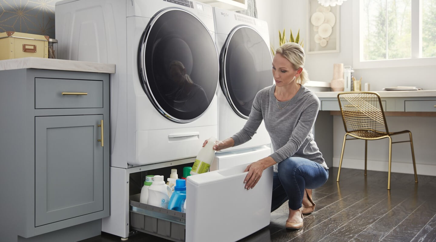 A woman putting laundry supplies in her Laundry Pedestal beneath her Whirlpool® Washer