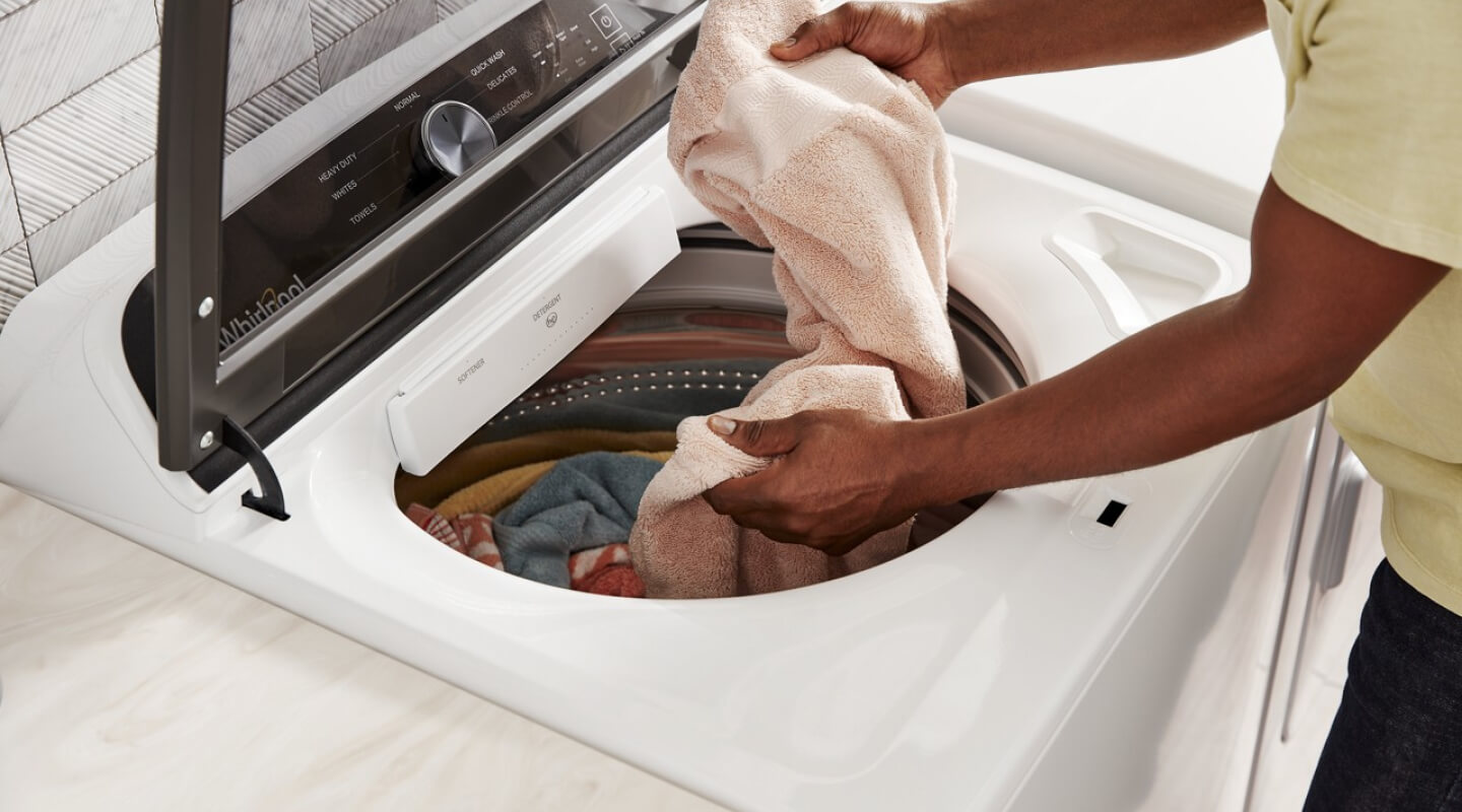 A person putting laundry into a white Whirlpool® Washing Machine A person putting laundry into a white Whirlpool® Washing Machine