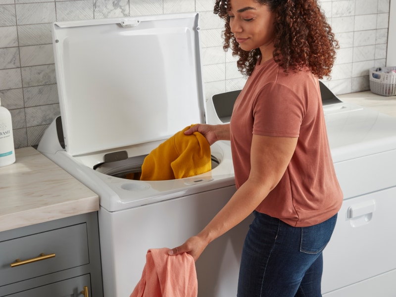 A woman puts clothes into a washer A woman puts clothes into a washer
