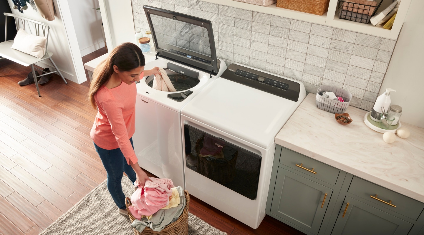 A woman putting a load of laundry into a top load washer A woman putting a load of laundry into a top load washer