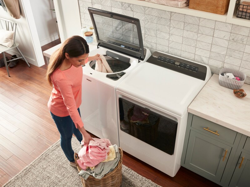 A woman putting a load of laundry into a top load washer A woman putting a load of laundry into a top load washer