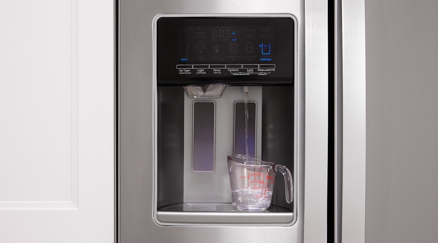 A measuring cup being filled with water from a side-by-side refrigerator's exterior dispenser