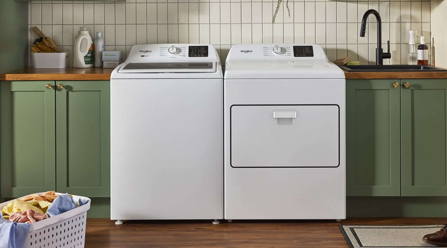 White Whirlpool® top load laundry pair in laundry room with green cabinetry