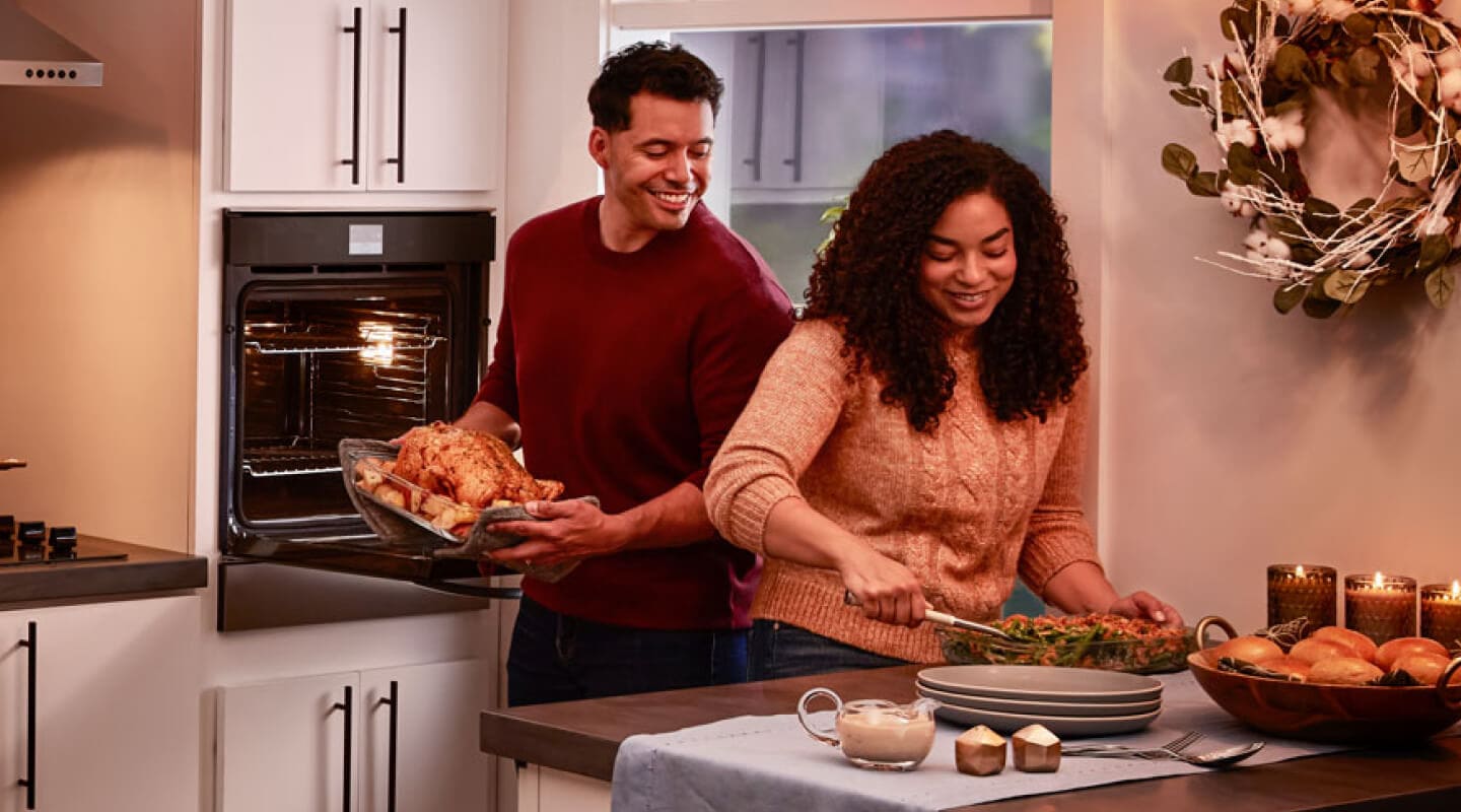 A couple preparing a dinner of roasted chicken, vegetables and bread rolls A couple preparing a dinner of roasted chicken, vegetables and bread rolls