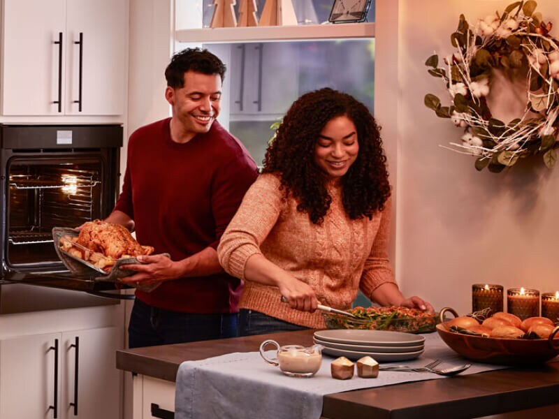 A couple preparing a dinner of roasted chicken, vegetables and bread rolls A couple preparing a dinner of roasted chicken, vegetables and bread rolls