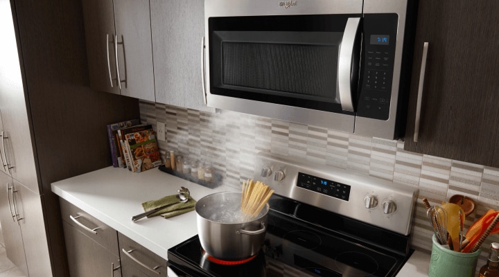 An over-the-range microwave with a pot of pasta cooking on the stove below An over-the-range microwave with a pot of pasta cooking on the stove below