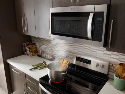 An over-the-range microwave with a pot of pasta cooking on the stove below An over-the-range microwave with a pot of pasta cooking on the stove below