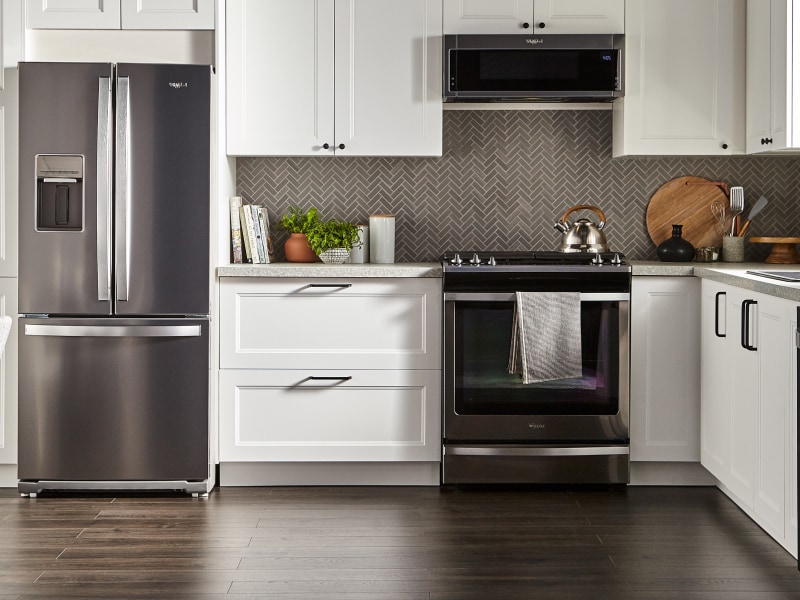Whirlpool oven and over-the-range microwave in a kitchen with gray herringbone tile backsplash and white cabinets. Whirlpool oven and over-the-range microwave in a kitchen with gray herringbone tile backsplash and white cabinets.