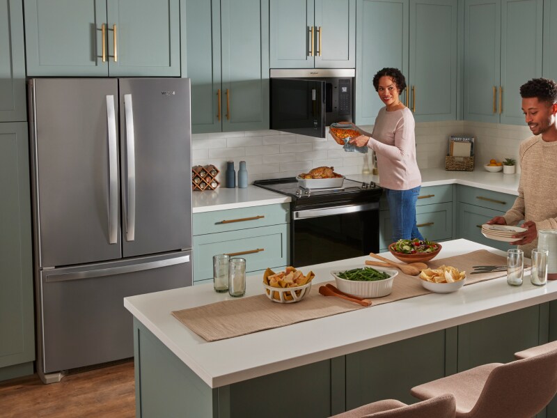 Two people cooking and preparing a meal in a kitchen with blue cabinets and white backsplash.  Two people cooking and preparing a meal in a kitchen with blue cabinets and white backsplash.