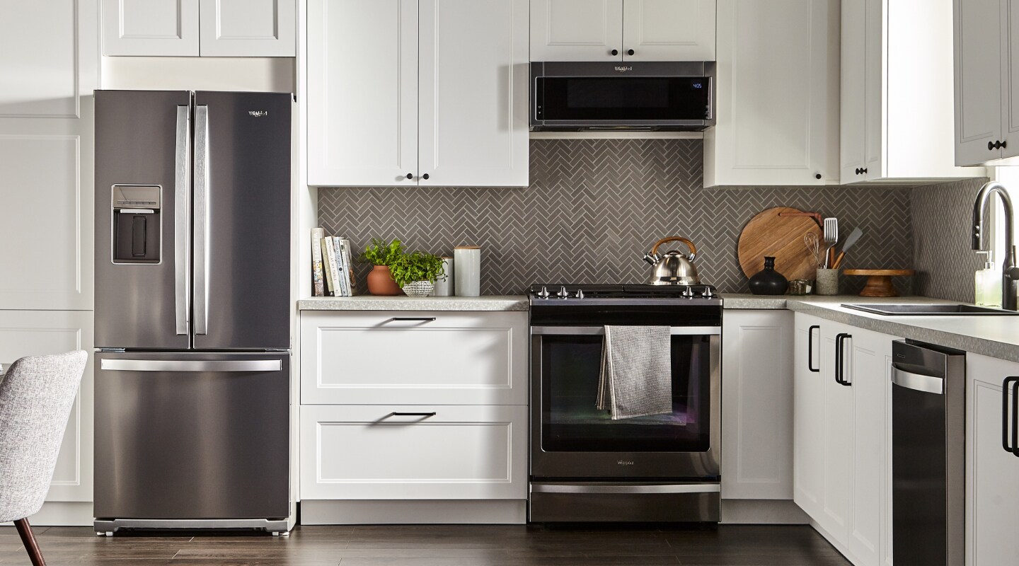 Whirlpool oven and over-the-range microwave in a kitchen with gray herringbone tile backsplash and white cabinets. Whirlpool oven and over-the-range microwave in a kitchen with gray herringbone tile backsplash and white cabinets.