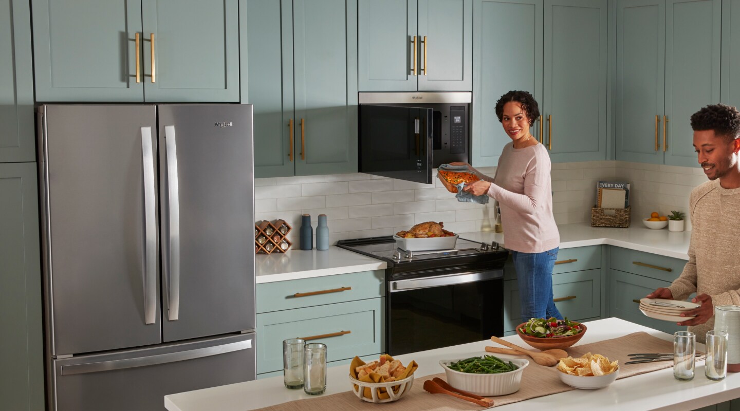 Two people cooking and preparing a meal in a kitchen with blue cabinets and white backsplash.  Two people cooking and preparing a meal in a kitchen with blue cabinets and white backsplash.