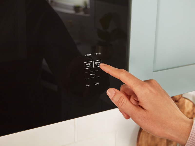 Person pressing start button on microwave